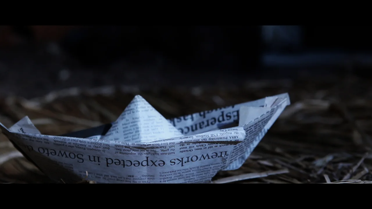 A newspaper folded into a paper boat, resting on straw